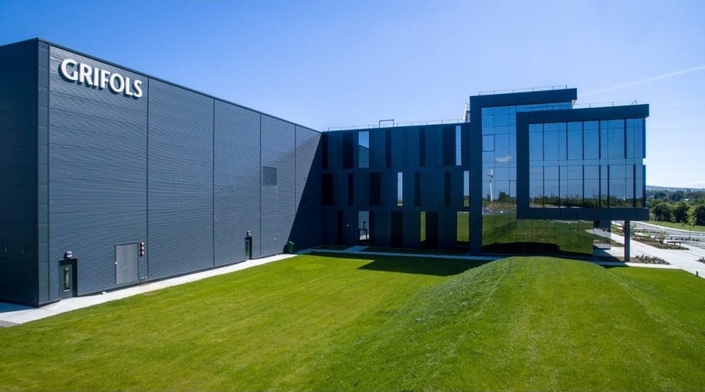 Image of a modern glass building with lush green lawn around it.