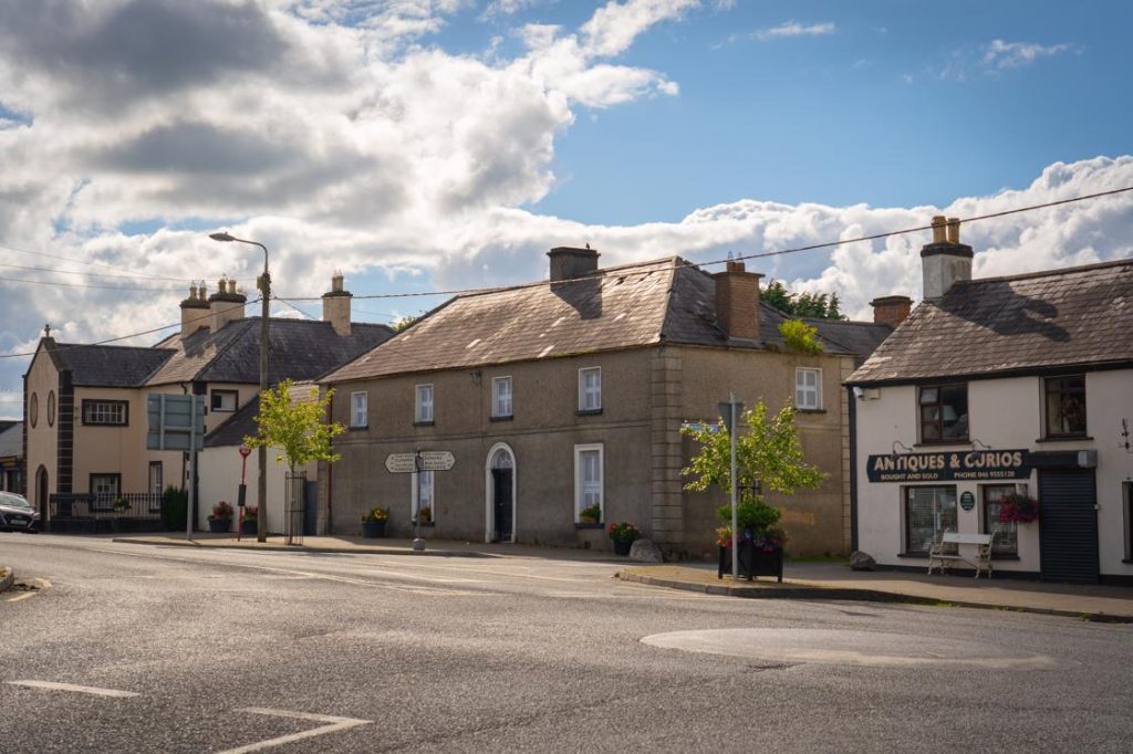 Image of a quiet street with a couple of buildings and a car parked by the side.
