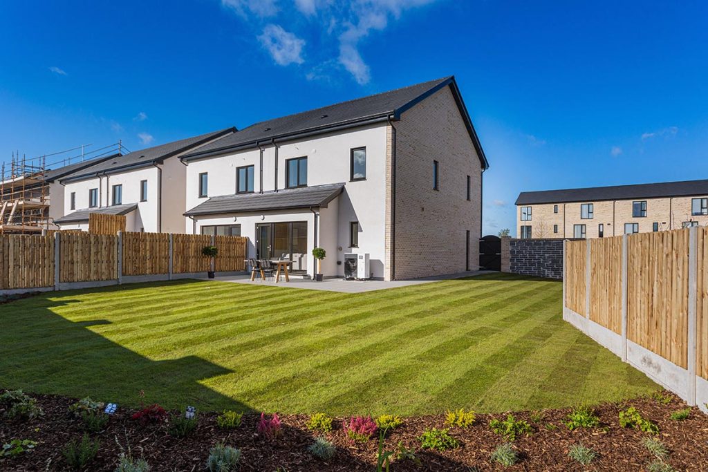 Image of a white semi-detached house with a well-maintained lawn enclosed by a fence, accompanied by a charming garden.
