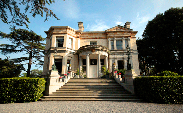 Image of an elegant beige house with a classic design, featuring multiple windows and a well-maintained exterior.
