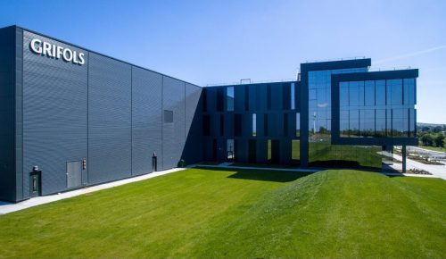 Image of a modern glass building with lush green lawn around it.