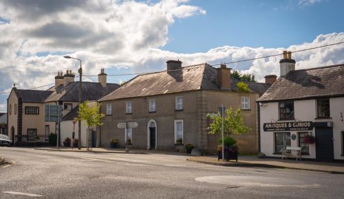 Image of a quiet street with a couple of buildings and a car parked by the side.