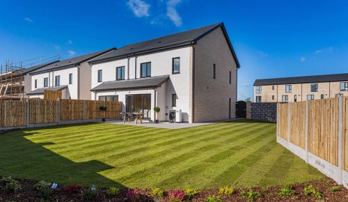 Image of a white semi-detached house with a well-maintained lawn enclosed by a fence, accompanied by a charming garden.