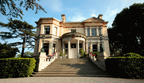Image of an elegant beige house with a classic design, featuring multiple windows and a well-maintained exterior.
